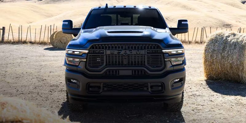 Front view of a black Ram Heavy Duty truck on a rural dirt road with hay bales in the background.