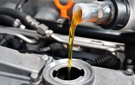 Close-up of fresh engine oil being poured into a vehicle engine during a routine oil change service.
