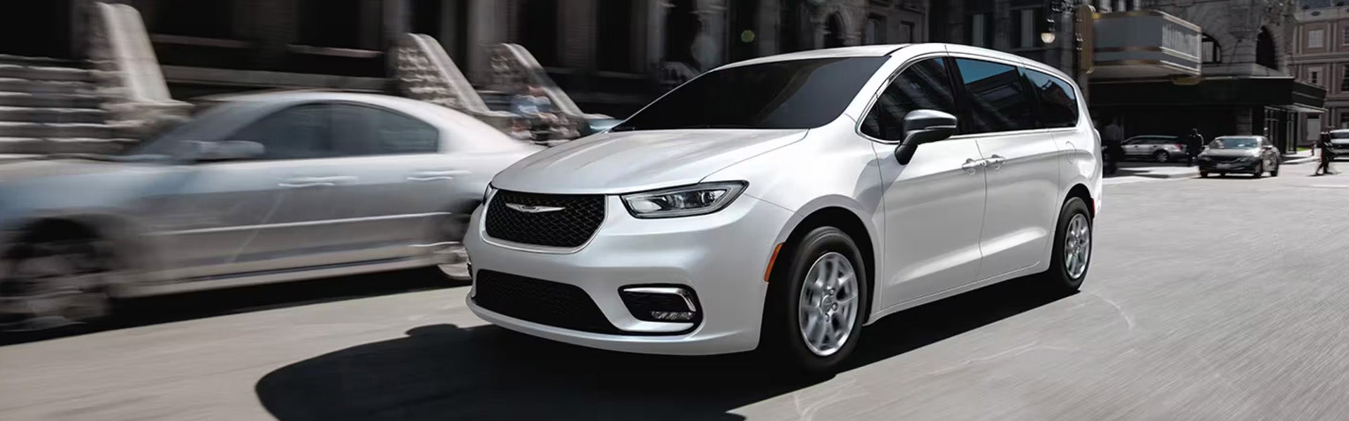 White Chrysler minivan driving through a city street.